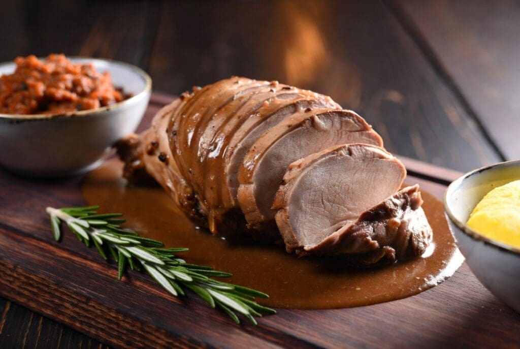 Tender carved lamb from a professional spit braai South Africa served with rich gravy, chakalaka and pap on a wooden board, premium catering presentation