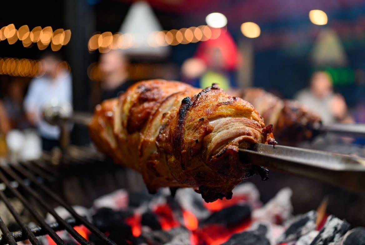 Close-up of crispy roasted meat on a spit braai at a birthday party, blurred festive background, food is the main focus, premium realistic style