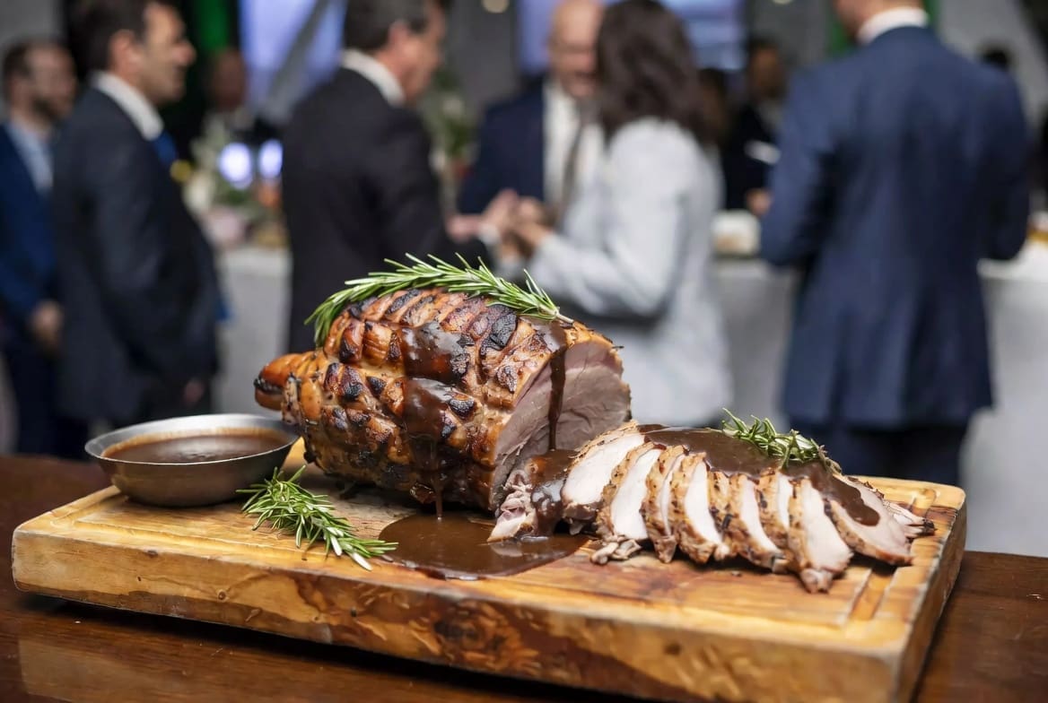 Sliced roasted meat from a spit braai served with gravy at a corporate event in Johannesburg, blurred business people in background, professional presentation