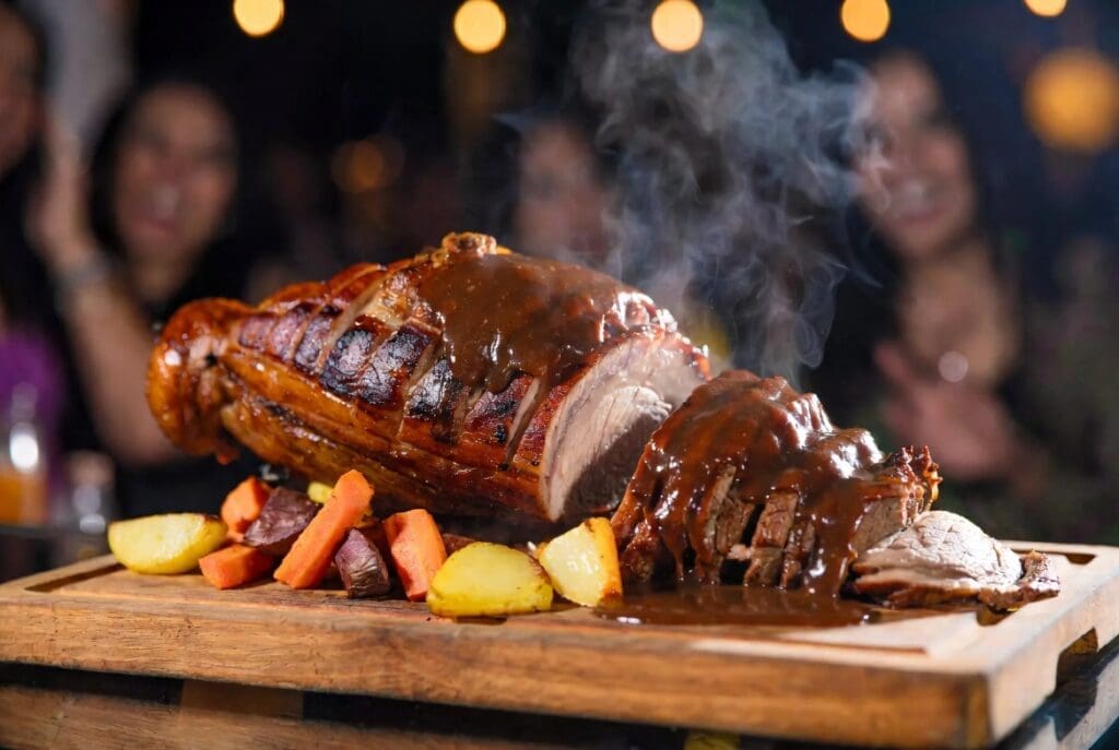 Sliced roasted meat from a spit braai served with gravy at a birthday party, blurred happy guests in background, professional party presentation