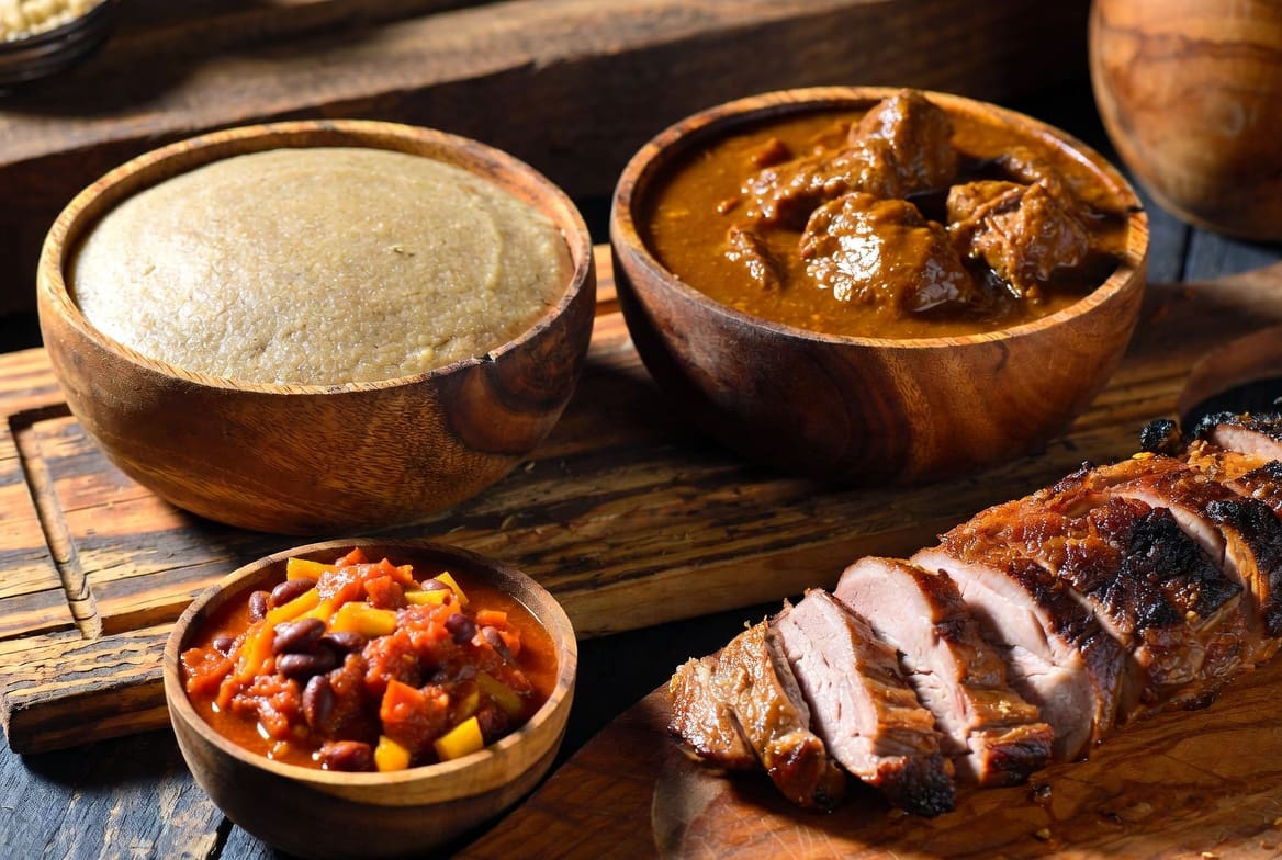 Close-up of classic African food cuisine dishes including pap, rich meat stew, chakalaka and spit-roasted meat