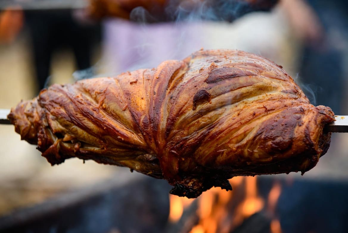 Close-up of crispy golden roasted meat on a spit braai catering spit with fire lighting, professional realistic food photography