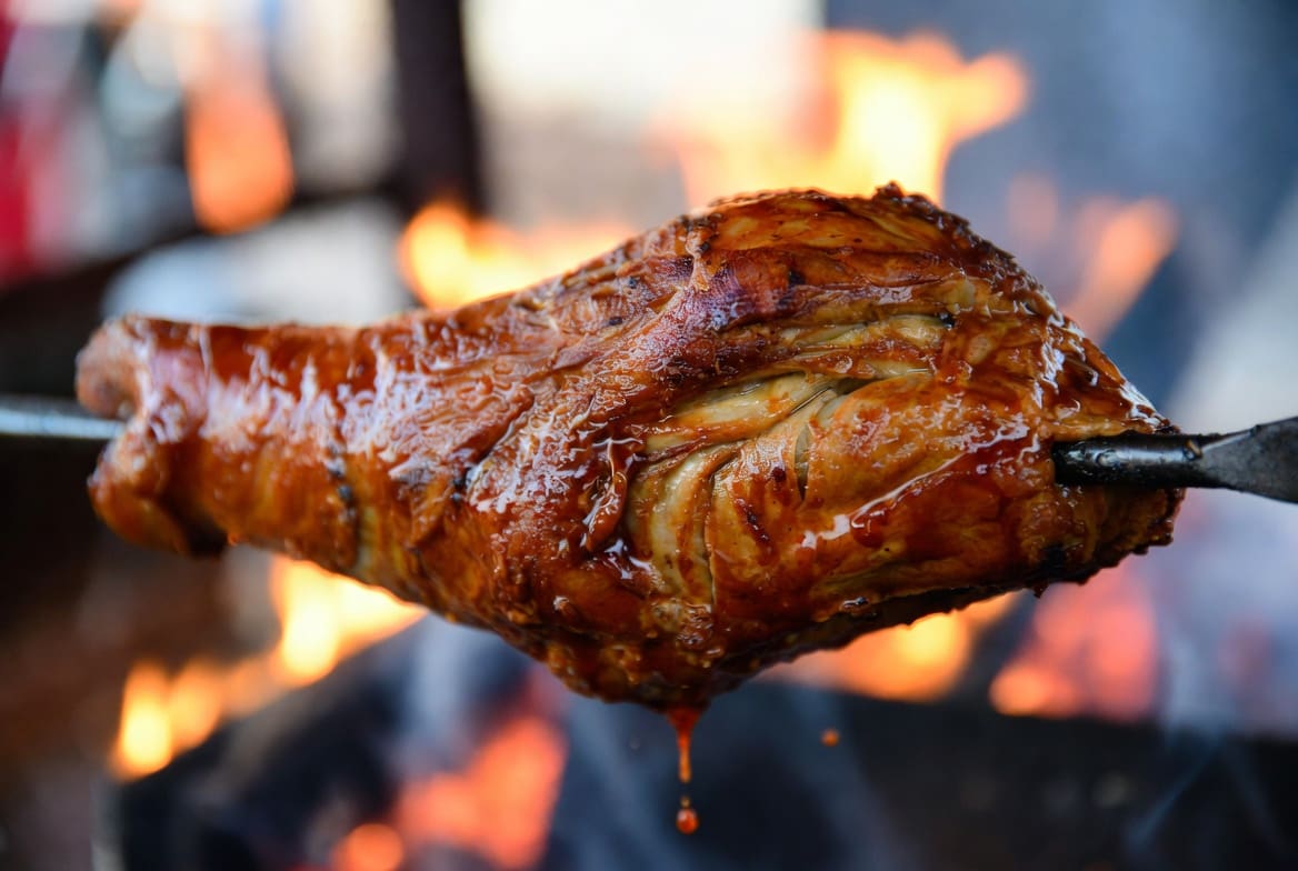 Close-up of crispy juicy roasted meat on a spitbraai catering spit with fire glow, professional local catering style