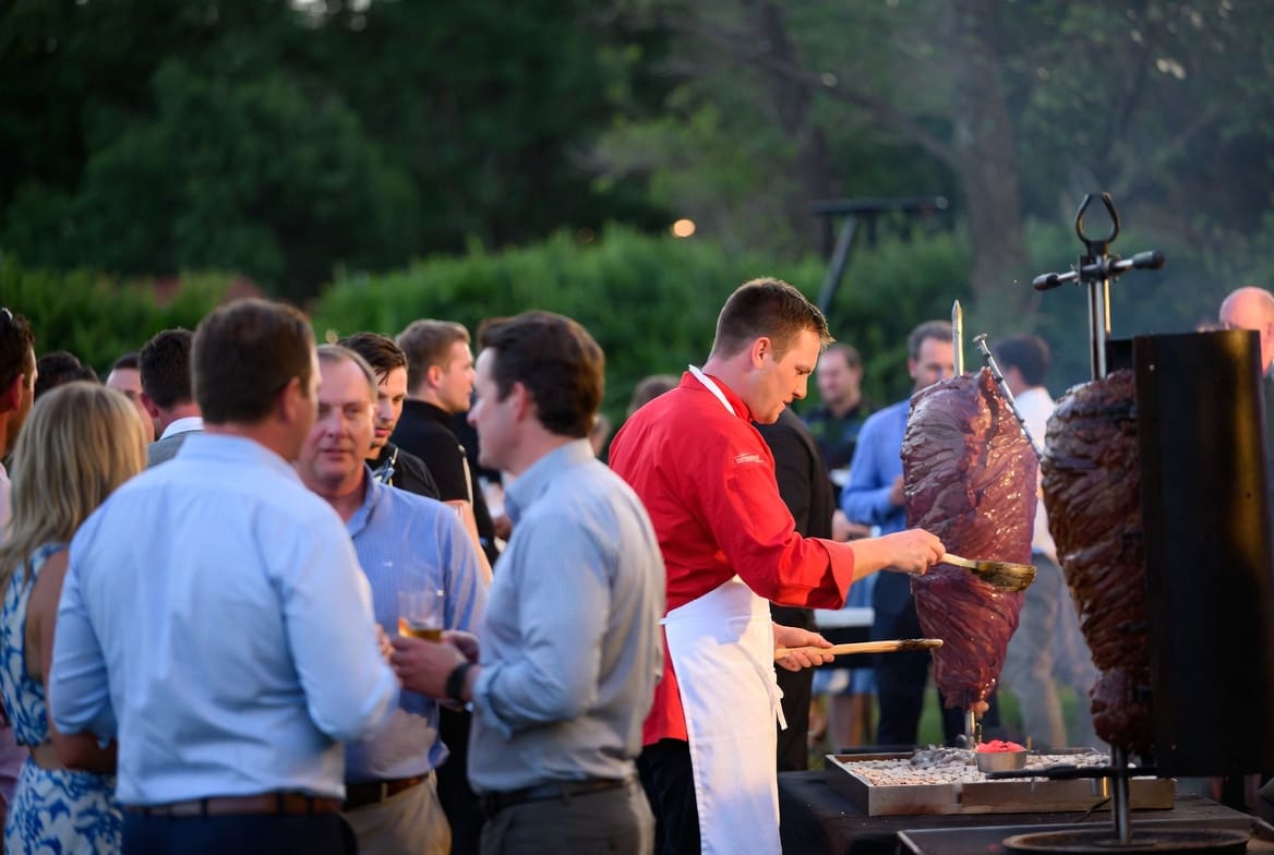 Corporate event with a chef in a red jacket basting the spit braai in the background.