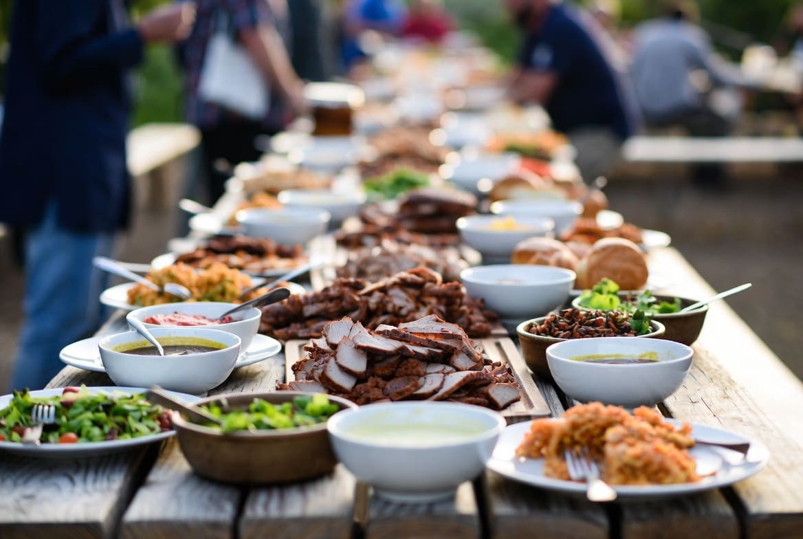 Long harvest table featuring sliced spit braai meat as the centrepiece with traditional sides and salads