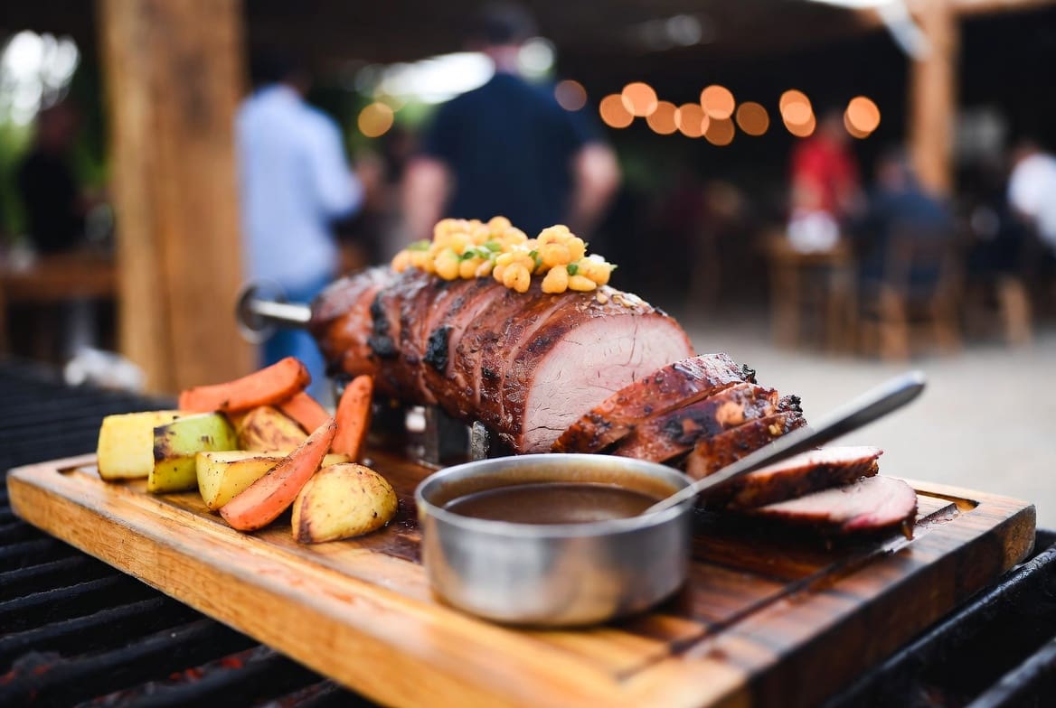 Carved spitbraai catering meat on a wooden board with gravy and roasted potatoes at a local South African event, food is the hero